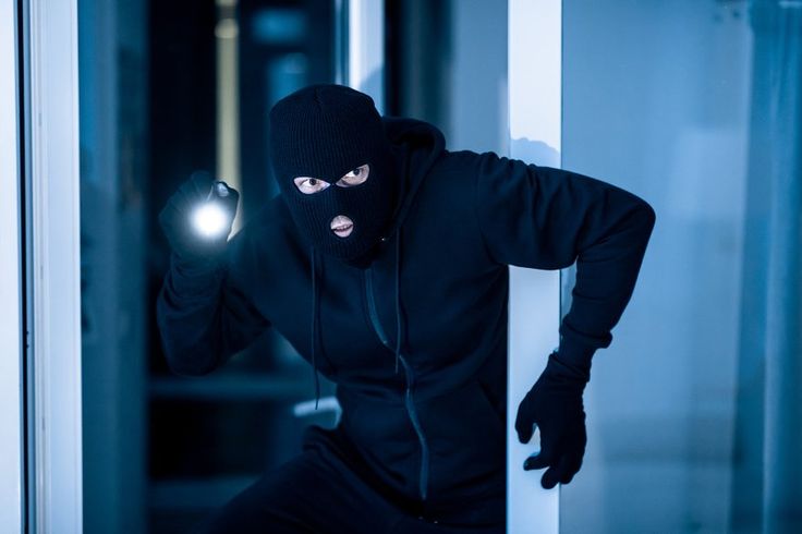 Masked intruder breaking into a building at night highlighting the need for business security devices